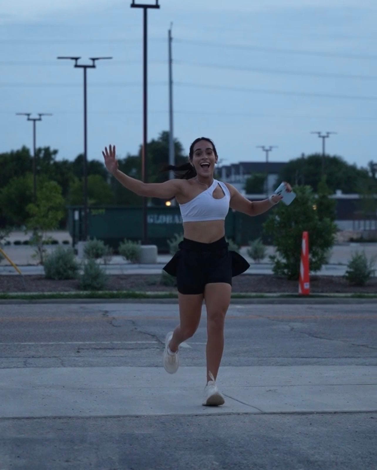 A runner smiling with both arms open at dusk
