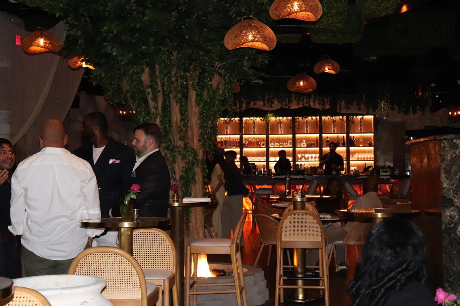 Guests mingling in a bar under a canopy of greenery and woven lamps