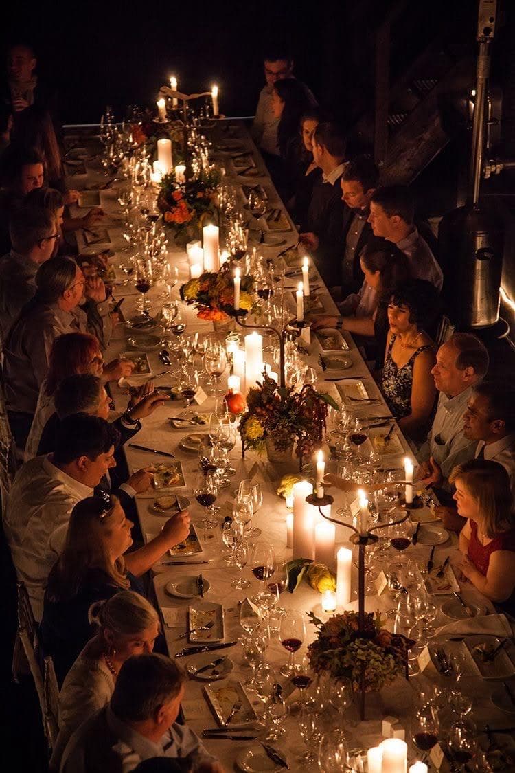 A long candlelit dinner table full of guests